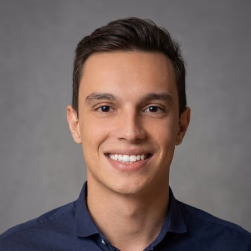 Close-up de homem jovem com cabelo cacheado escuro e camiseta azul sorrindo levemente.